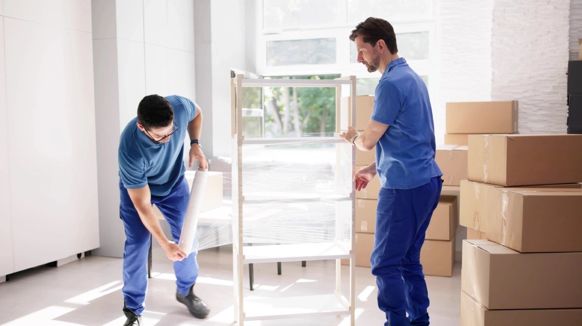 Two movers wrapping a piece of furniture with a clear wrap.